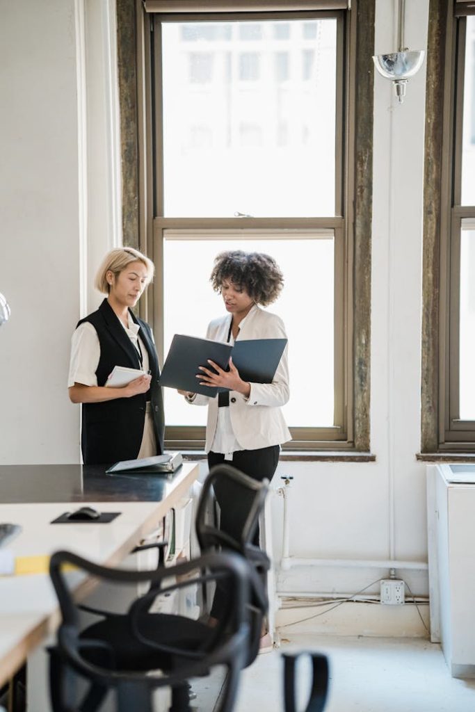 Two women discussing work in a bright, modern office setting.